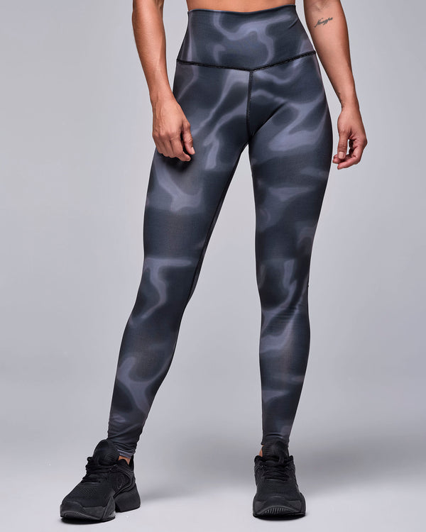 The black and grey swirl print leggings on a female model, with a high, smooth waistband and a fitted ankle-length leg, paired with black shoes.