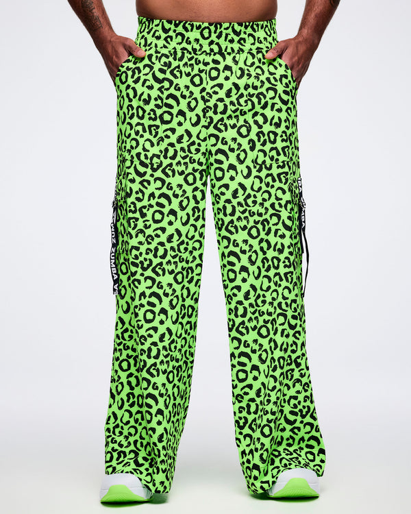 Male model wearing neon green leopard print cargo pants with hands in both side pockets.
