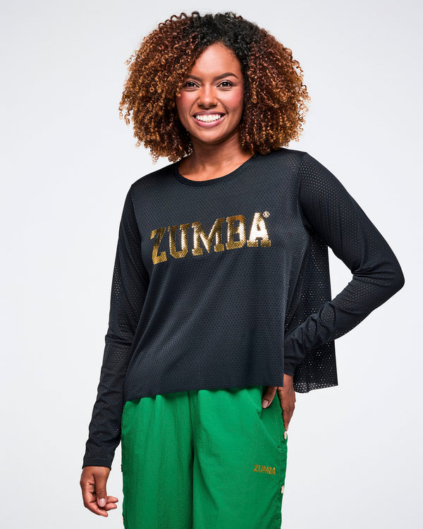 Female model wearing a black Zumba mesh top with gold 'ZUMBA' lettering in the center, paired with green pants on a white background.