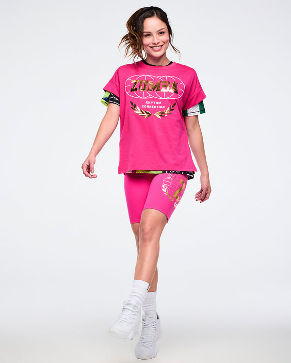 Female model wearing a pink top and pink biker shorts with white socks and shoes against a white background.