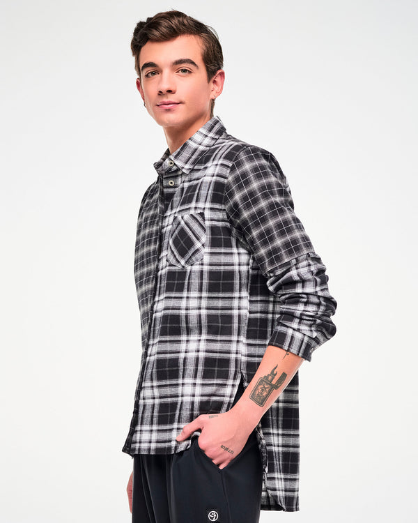Side view of a male model wearing a long-sleeve button-up plaid shirt with a black, white, and gray checkered pattern, paired with black pants.