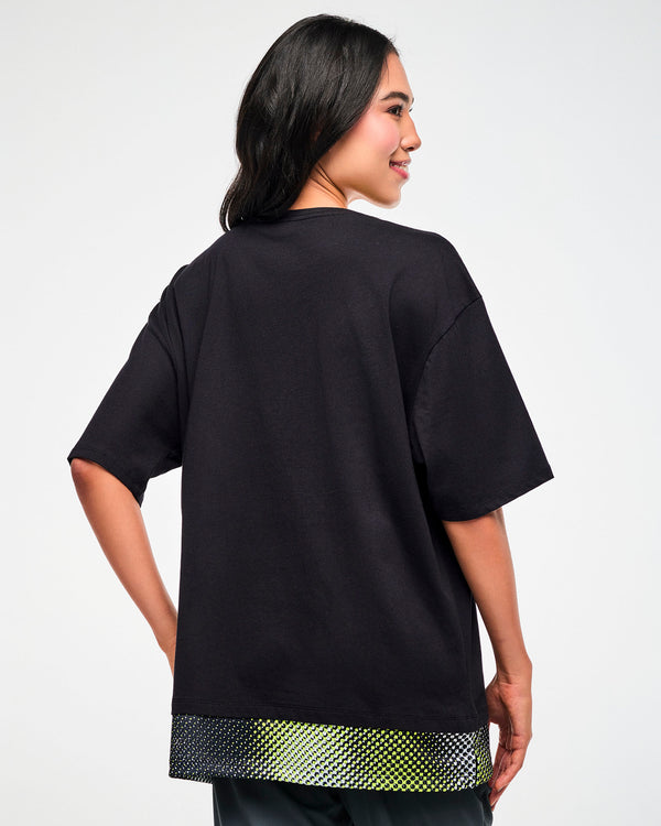Back view of a female model wearing a black oversized T-shirt with a yellow, black, and white mesh dot-print hem.