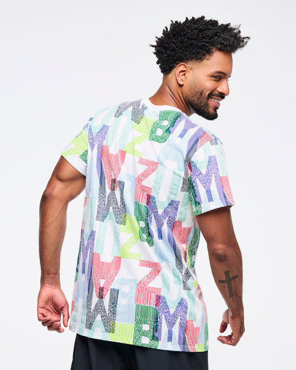 Back view of the all-over multicolor “ZUMBA” print T-shirt on a male model, showing the continuous graphic pattern and straight hem, paired with black pants.