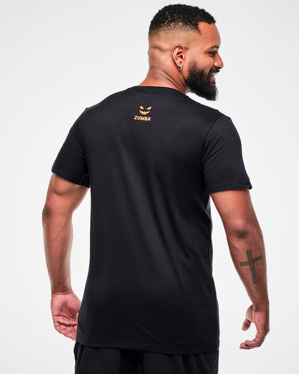Shown from the back, male model wearing a black tee with a small orange jack-o'-lantern graphic and
