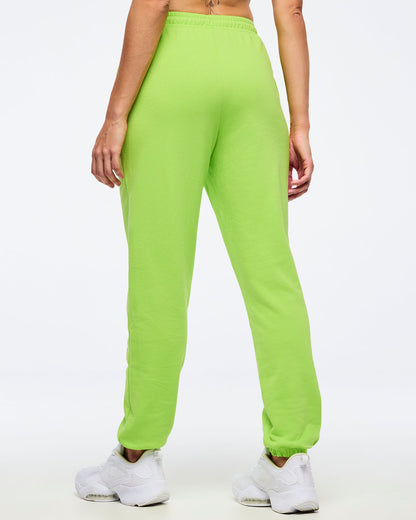 Back view of neon green Zumba joggers with elastic waistband and tapered ankles, worn by a female model with white sneakers.