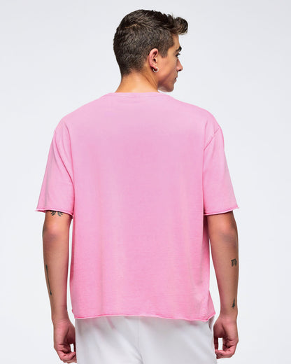 Back view of a pink pastel relaxed-fit crewneck T-shirt with dropped shoulders and elbow-length sleeves, worn by a male model with white shorts against a light studio background.