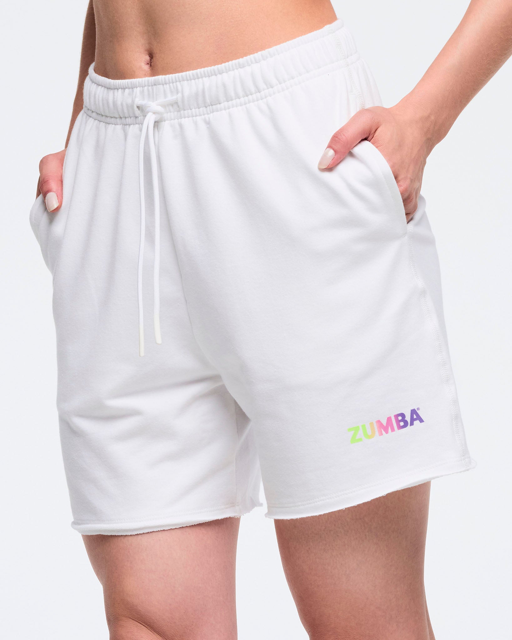 Close up of woman in white shorts, with hands in her pockets. Zumba text in pastel colors on the left leg and the model on a white background.
