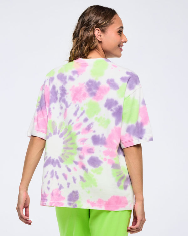 Back view of a woman on a white background wearing an oversized pastel  patterned tie-dye T-shirt with pink, purple, and lime green splashes, paired with bright lime green pants.
