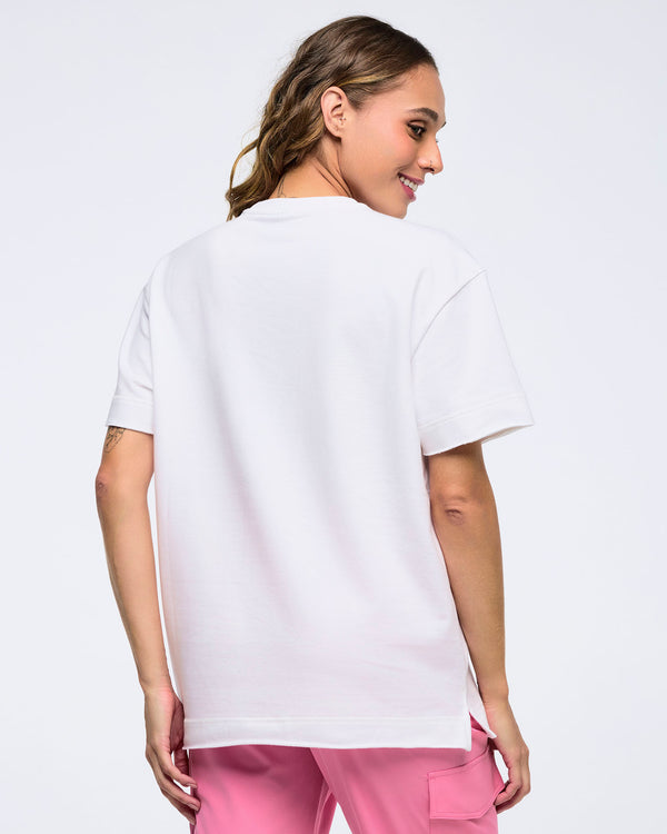Back view of a woman on a white background wearing a plain white T-shirt and pink pants, turned slightly to the side and smiling.