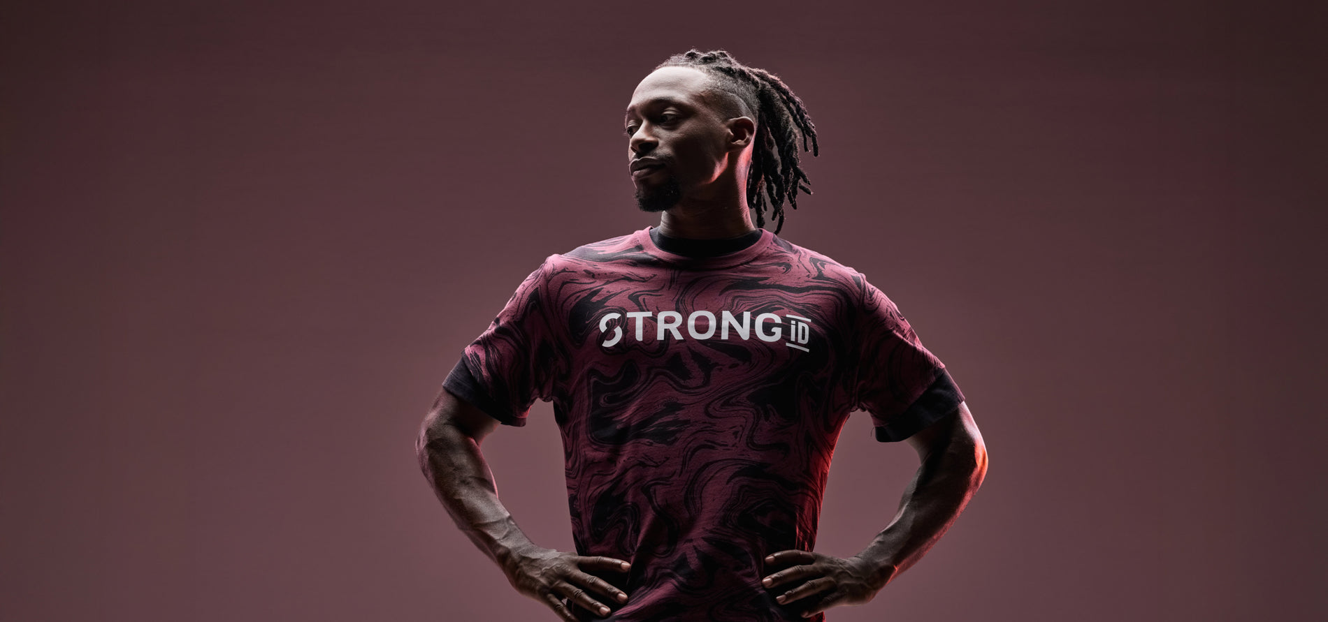 Banner showing a male model against a mauve gradient studio background with hands on his hips. He wears a burgundy and black marbled short-sleeve athletic T-shirt with “STRONG iD” printed in bold across the chest.
