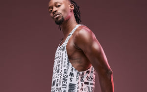 A male model in a white graphic Zumba tank top poses confidently against a maroon background.