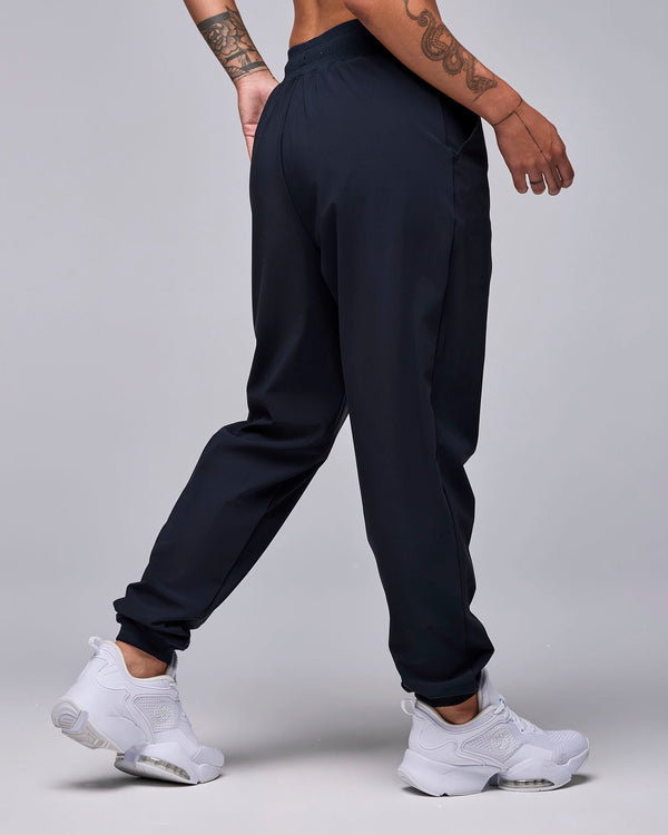 Shown from the back, the black high-waisted joggers with a relaxed fit through the seat and legs, gathering at elastic cuffs above white shoes.