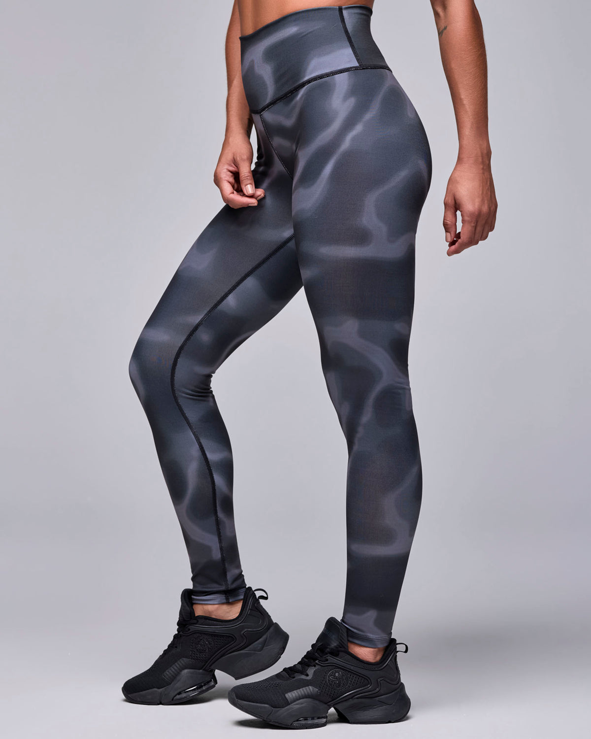 Female model in high-waisted ankle leggings with a black and grey swirl print and a smooth, wide waistband, shown in side view with black shoes.