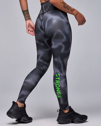Back view of a female model in the black and grey swirl print leggings, with neon green 'STRONG iD' text running down the back of the right calf.