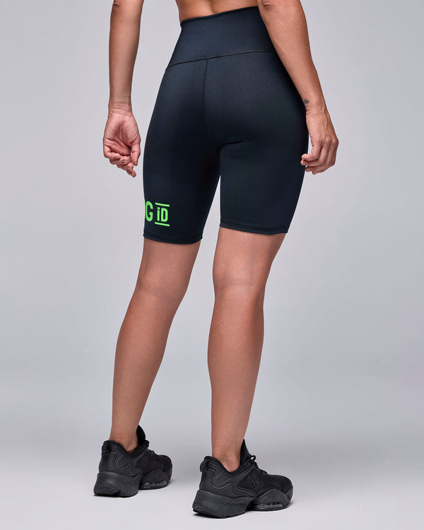 Back view of a female model in the black biker shorts, with the end of the neon green 'STRONG iD' text on the back of the left leg.