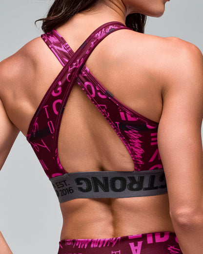 Close up back view of the burgundy and pink graphic-print sports bra with crisscross back straps and a gray elastic under-band, on a female model.