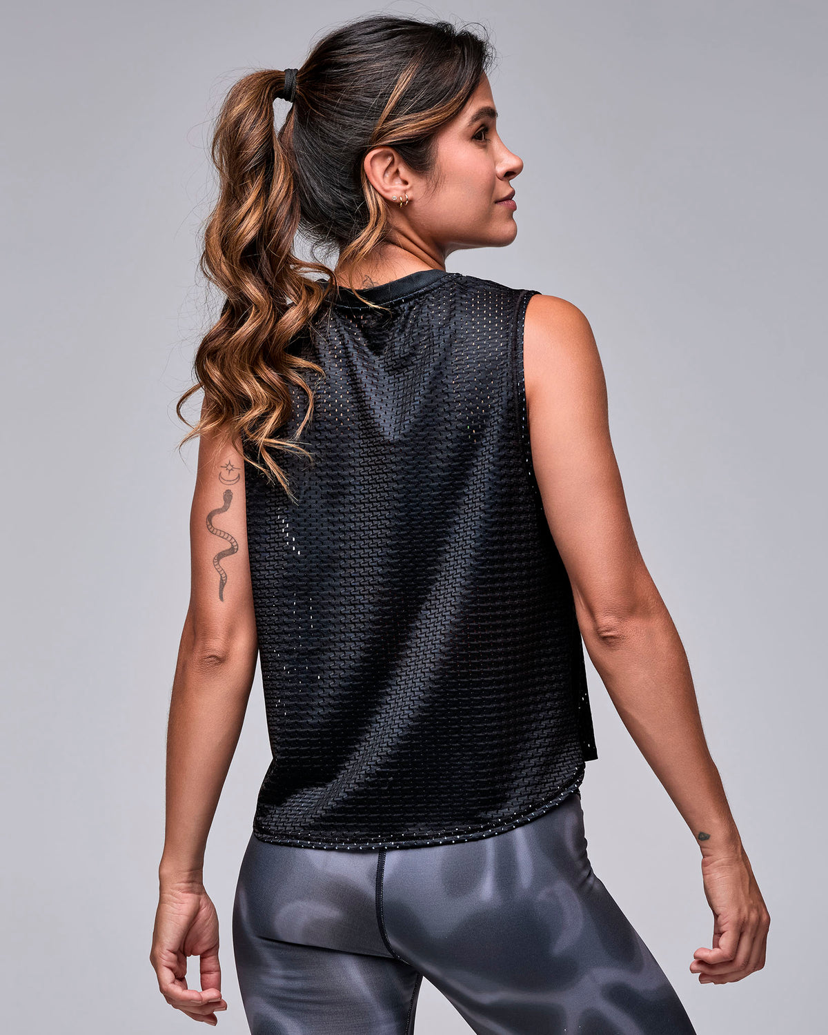 Shown from the back, the black loose mesh 'STRONG iD' muscle tank, with a plain open-hole mesh back and relaxed fit over black and grey swirl print leggings.