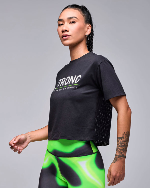 Black cropped boxy 'STRONG' top on a female model, shown in side view, with a glimpse of the mesh back panel along the side.