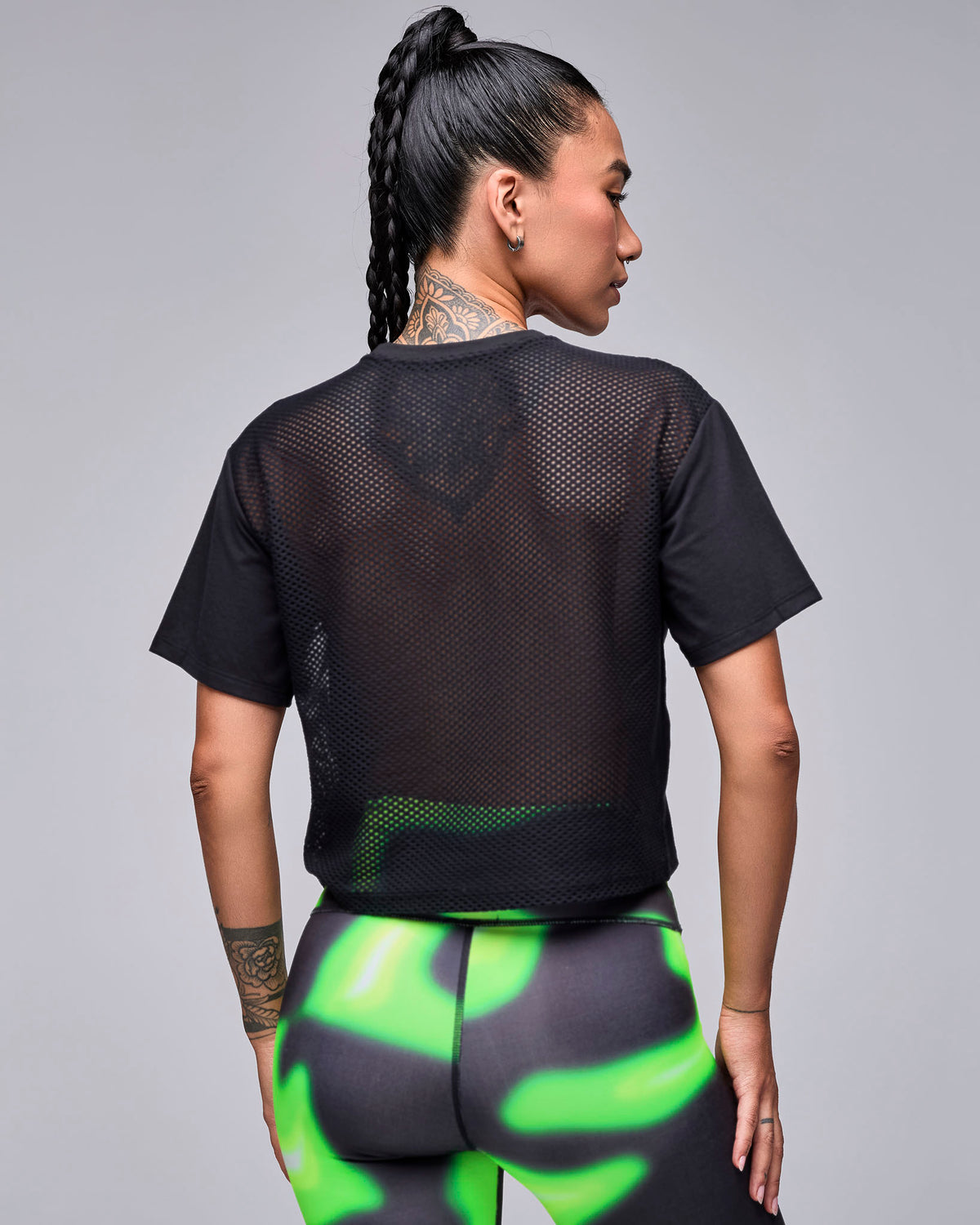 Shown from the back, the black 'STRONG' boxy top's sheer mesh back panel, with neon green and black swirl print leggings.