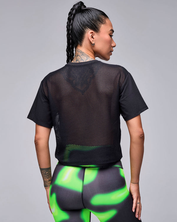 Shown from the back, the black 'STRONG' boxy top's sheer mesh back panel, with neon green and black swirl print leggings.