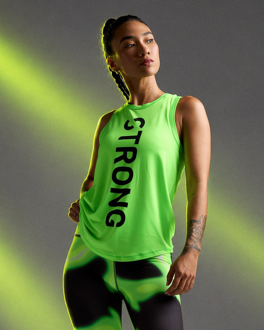 Female model in a neon green basketball tank with a curved hem and vertical black 'STRONG' text down the front, paired with neon green and black swirl print leggings, against neon light beams.