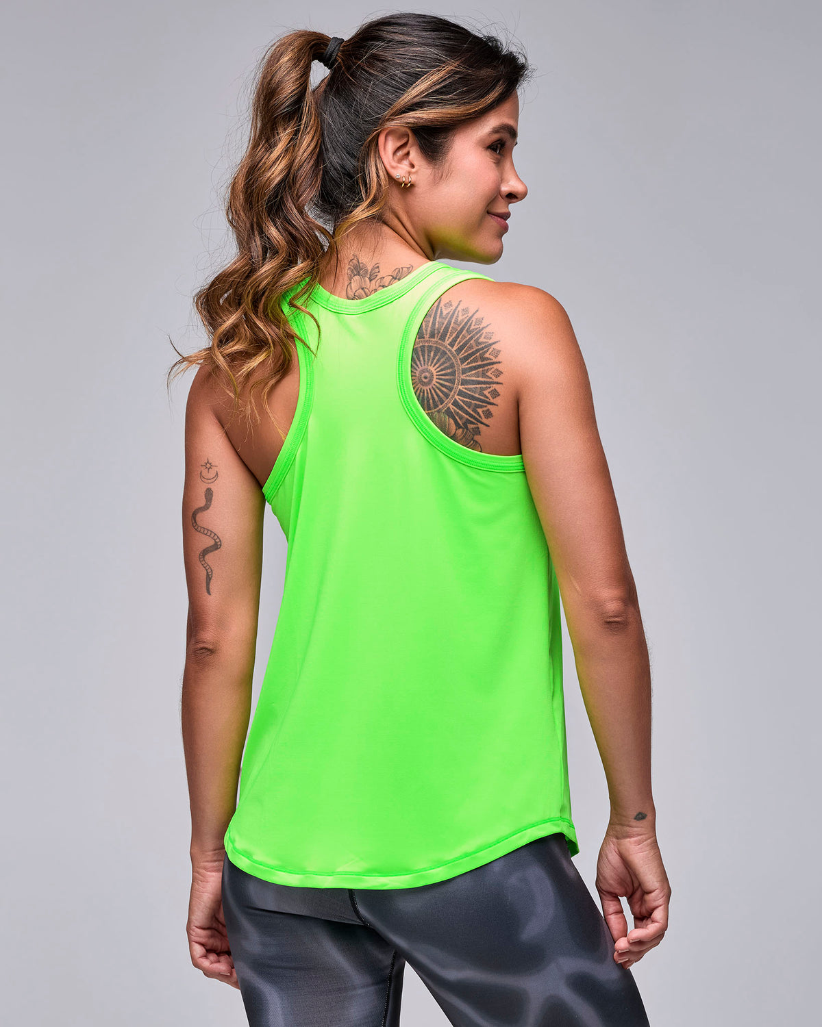 Shown from the back, the neon green 'STRONG' basketball tank with a racerback and plain back, over black and grey swirl print leggings.