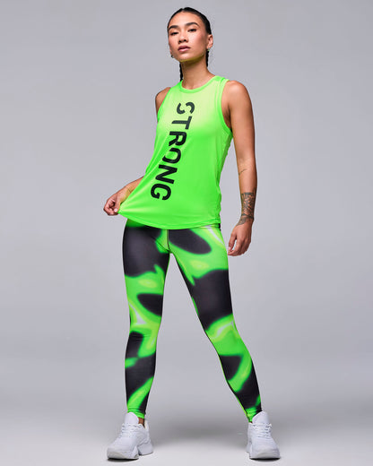 Full view of a female model in the neon green 'STRONG' basketball tank with neon green and black swirl print leggings and white shoes.