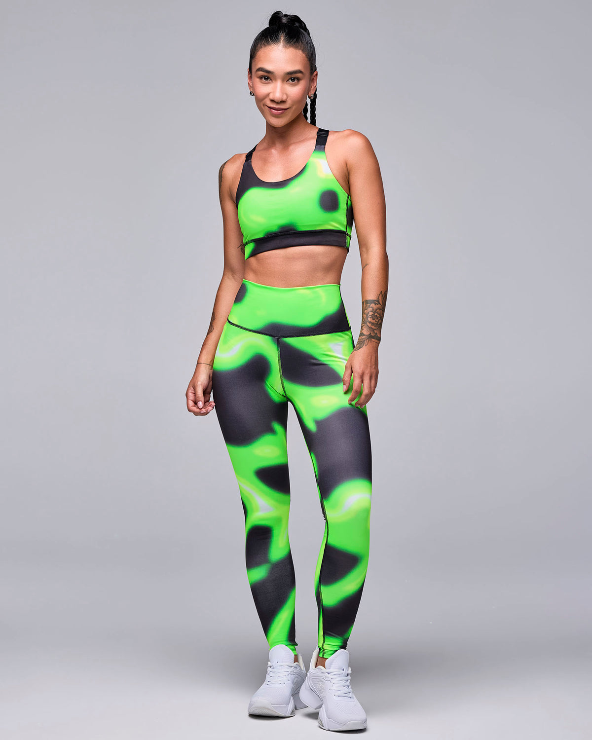 Full view of a female model in the neon green and black swirl print bra with matching leggings and white shoes.