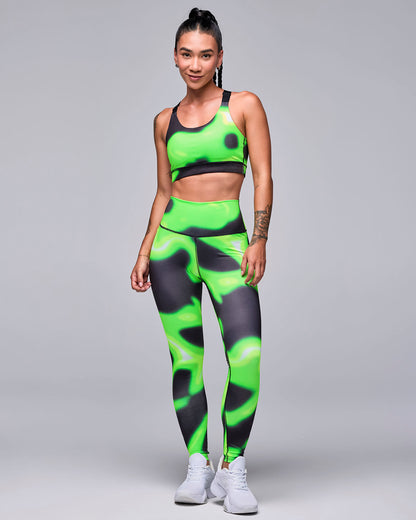 Full view of a female model in the neon green and black swirl print bra with matching leggings and white shoes.