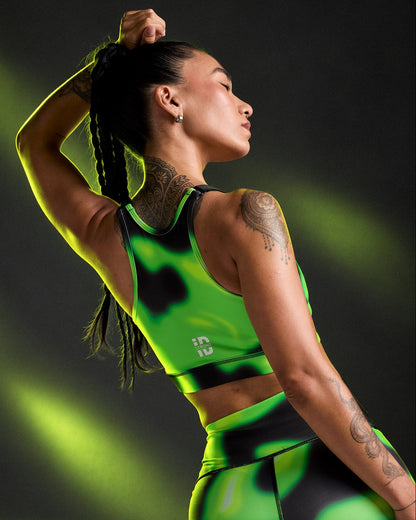 Shown from the back, a female model with one arm overhead in the swirl print bra and matching leggings, the white 'STRONG iD' logo near the band, under neon light beams.