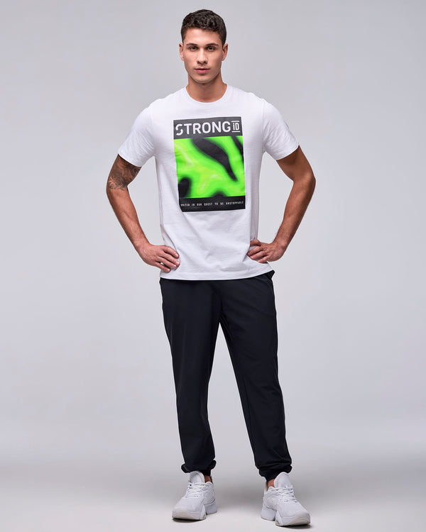 Full view of a male model in the white 'STRONG iD' graphic tee with black joggers and white shoes, hands on hips.