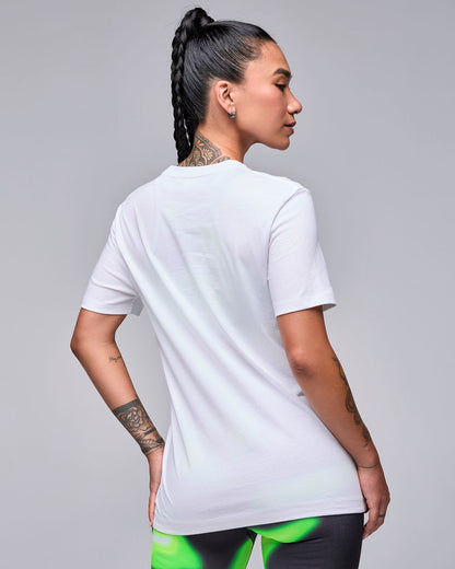 Back view of a female model in the white 'STRONG iD' graphic tee, showing a plain back and relaxed fit, with swirl print leggings.