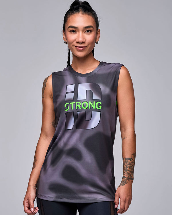 Female model in the black and grey swirl print wide shoulder tank with the large grey 'iD' graphic and neon green 'STRONG' text, worn loose over black leggings.