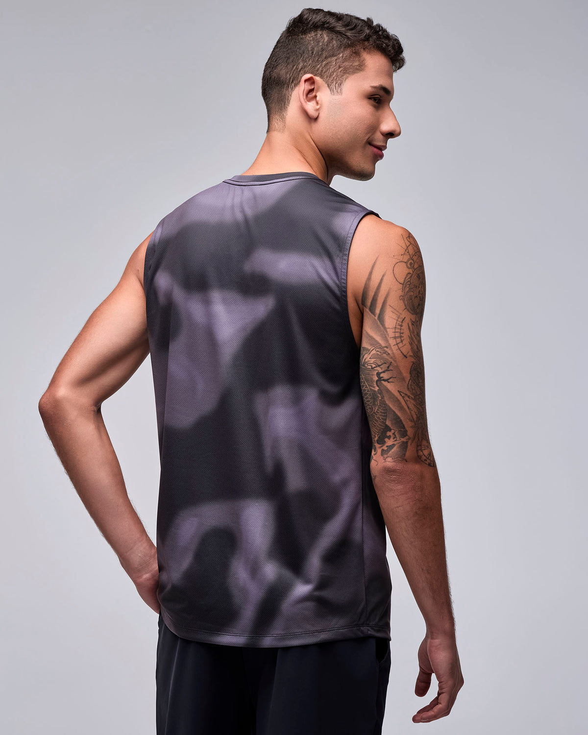 Back view of the black and grey swirl print wide shoulder tank on a male model, plain on the back with wide armholes.