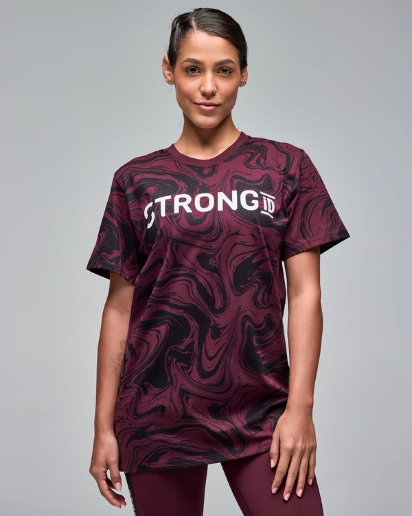 Maroon and black swirl-print graphic T-shirt with bold white “STRONG iD” lettering across the chest. Female model wears the short-sleeve crewneck tee in a close-up view against a light gray background.