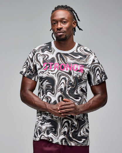 White and black swirl-print graphic T-shirt with bright pink “STRONG iD” text on the chest. Male model wears the short-sleeve crewneck tee with burgundy athletic shorts, standing against a light gray background.