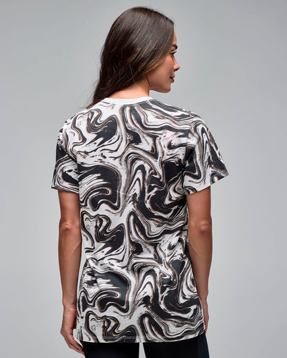 Back view of a white and black swirl-print short-sleeve T-shirt. Female model wears the crewneck tee with black leggings, showing the all-over abstract pattern on the back against a light gray background.