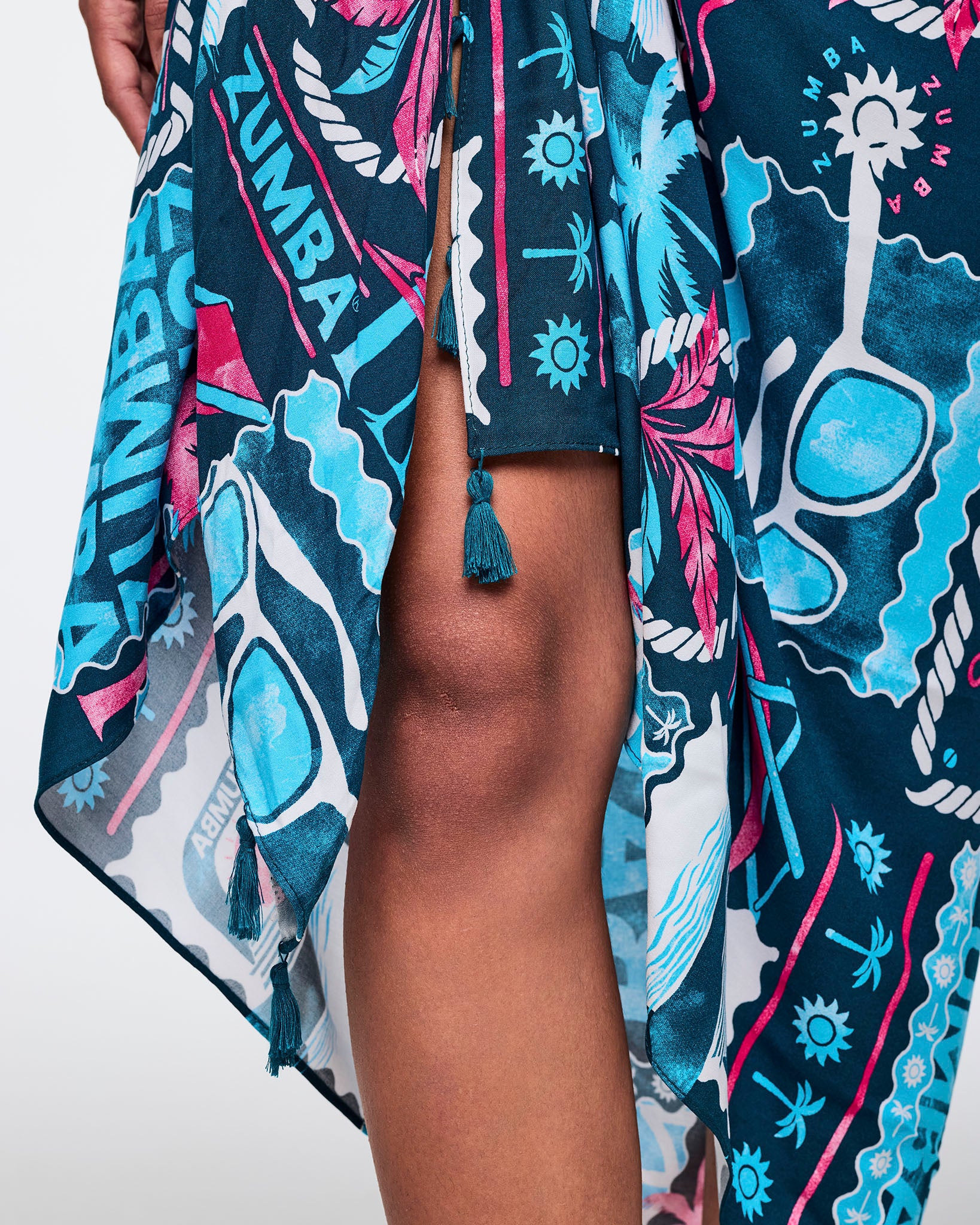 Close-up of the navy Zumba sarong tie detail showing the front knot, tassel ends, and bold teal-and-pink tropical graphic print.