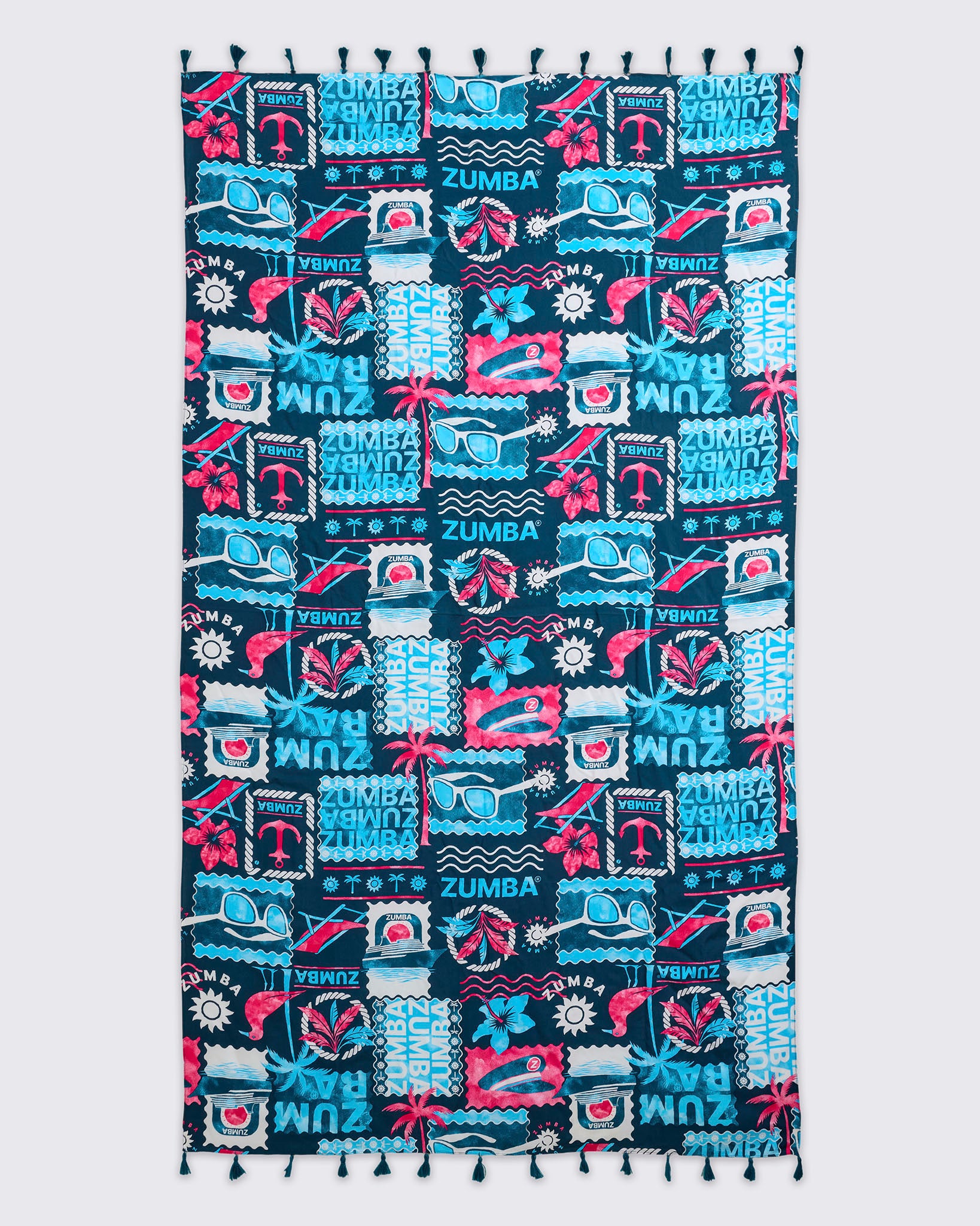 Navy Zumba beach blanket or towel with tassel trim and an allover teal-and-pink tropical collage print featuring sunglasses, flowers, waves, and logos, laid flat.
