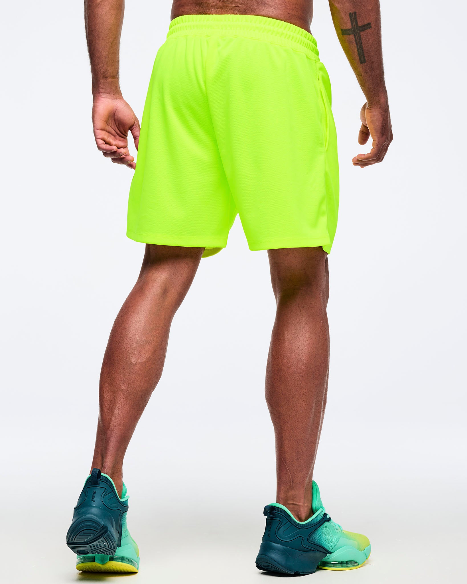 Neon lime athletic shorts with an elastic waistband and relaxed fit, shown from the back on a male model wearing teal-to-lime athletic sneakers on a white studio background.