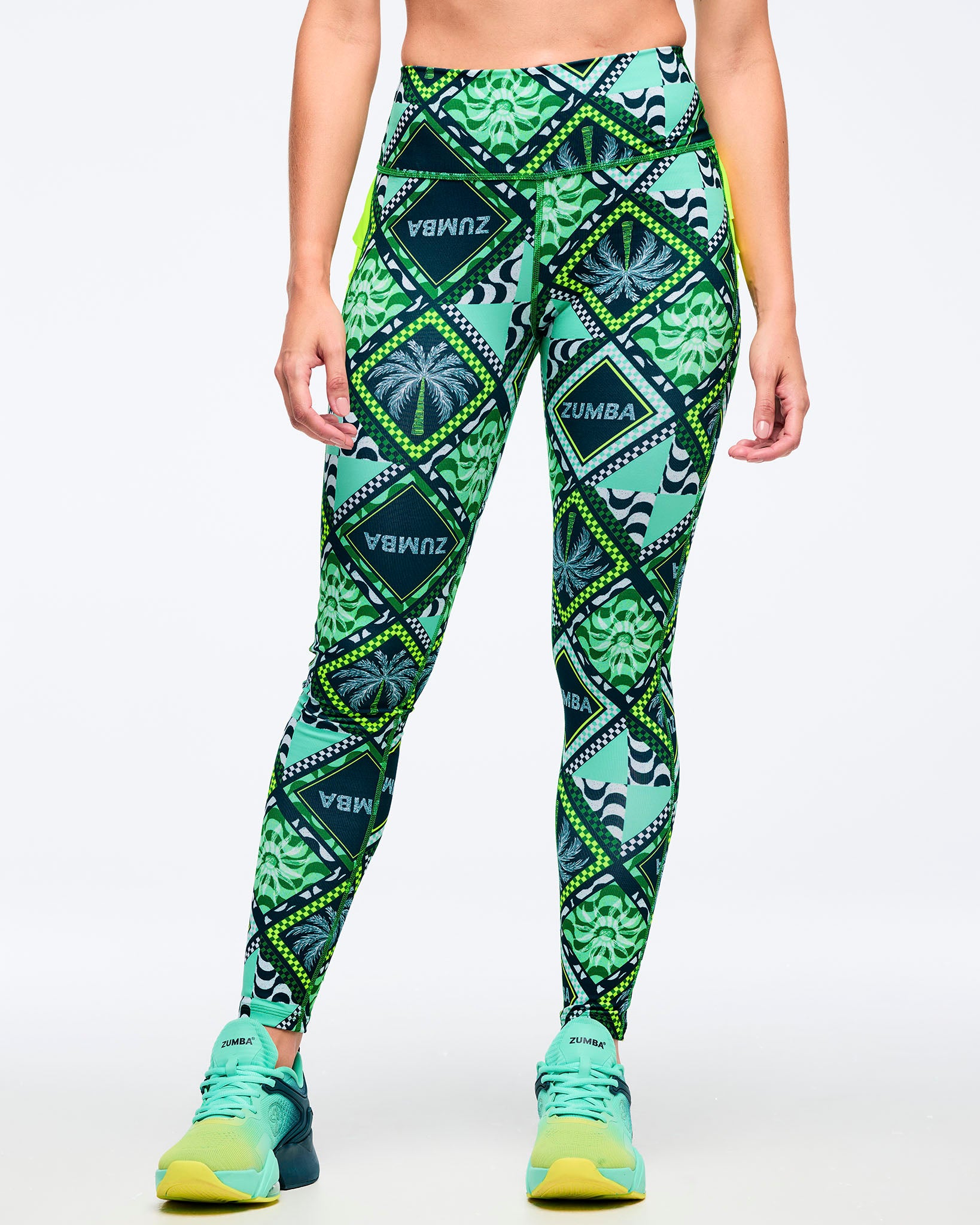 Green geometric-print high-waisted leggings with a smooth wide waistband and allover diamond-and-leaf pattern, shown from the front on a female model wearing teal-to-lime athletic sneakers on a white studio background.