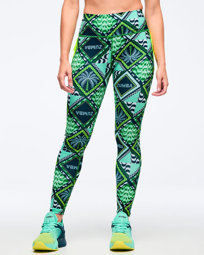 Green geometric-print high-waisted leggings with a smooth wide waistband and allover diamond-and-leaf pattern, shown from the front on a female model wearing teal-to-lime athletic sneakers on a white studio background.