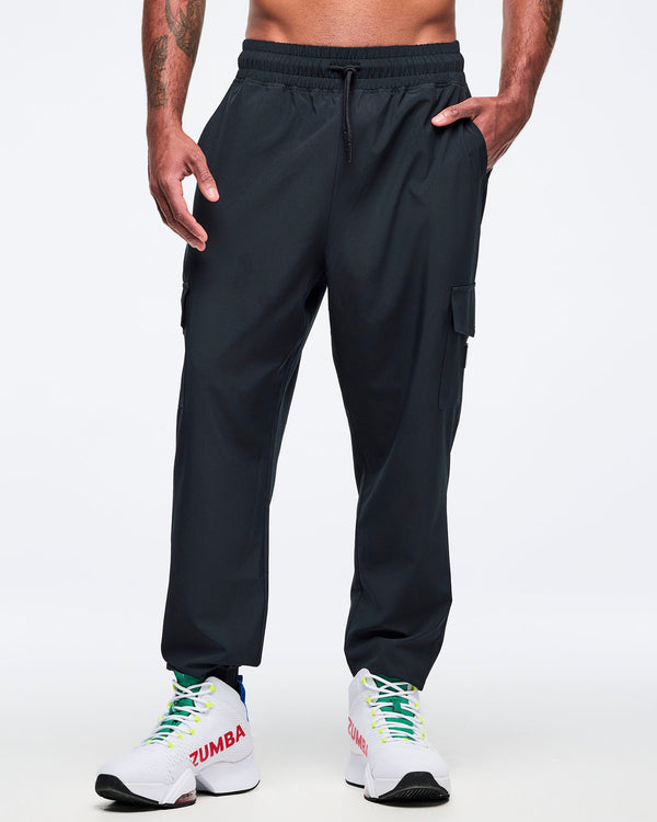 Black cargo jogger pants shown from the front on a male model; elastic drawstring waistband, cargo pocket details, and tapered ankles, paired with white high-top Zumba sneakers.