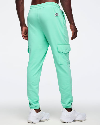 Mint green cargo jogger pants shown from the back on a male model; elastic waistband, relaxed legs, and right thigh flap cargo pocket, paired with white sneakers.