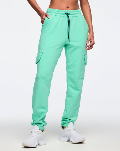 Mint green cargo jogger pants with an elastic drawstring waistband, side pockets, and flap cargo pockets on both thighs, worn by a female model with white low-top sneakers.