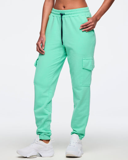 Mint green cargo jogger pants with a dark drawstring and thigh cargo pockets, shown from the front on a female model; relaxed fit with ankle cuffs, paired with white sneakers.