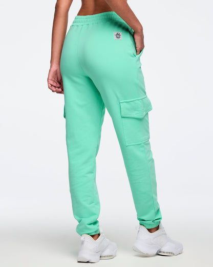 Mint green cargo jogger pants shown from the back on a female model; elastic waistband, tapered legs with ankle cuffs, and a right thigh flap cargo pocket, paired with white sneakers.