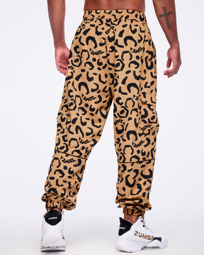 Tan leopard-print cargo pants with black abstract spots and logo accents, shown from the back on a male model wearing white high-top Zumba sneakers with black heel panels and leopard-print details.
