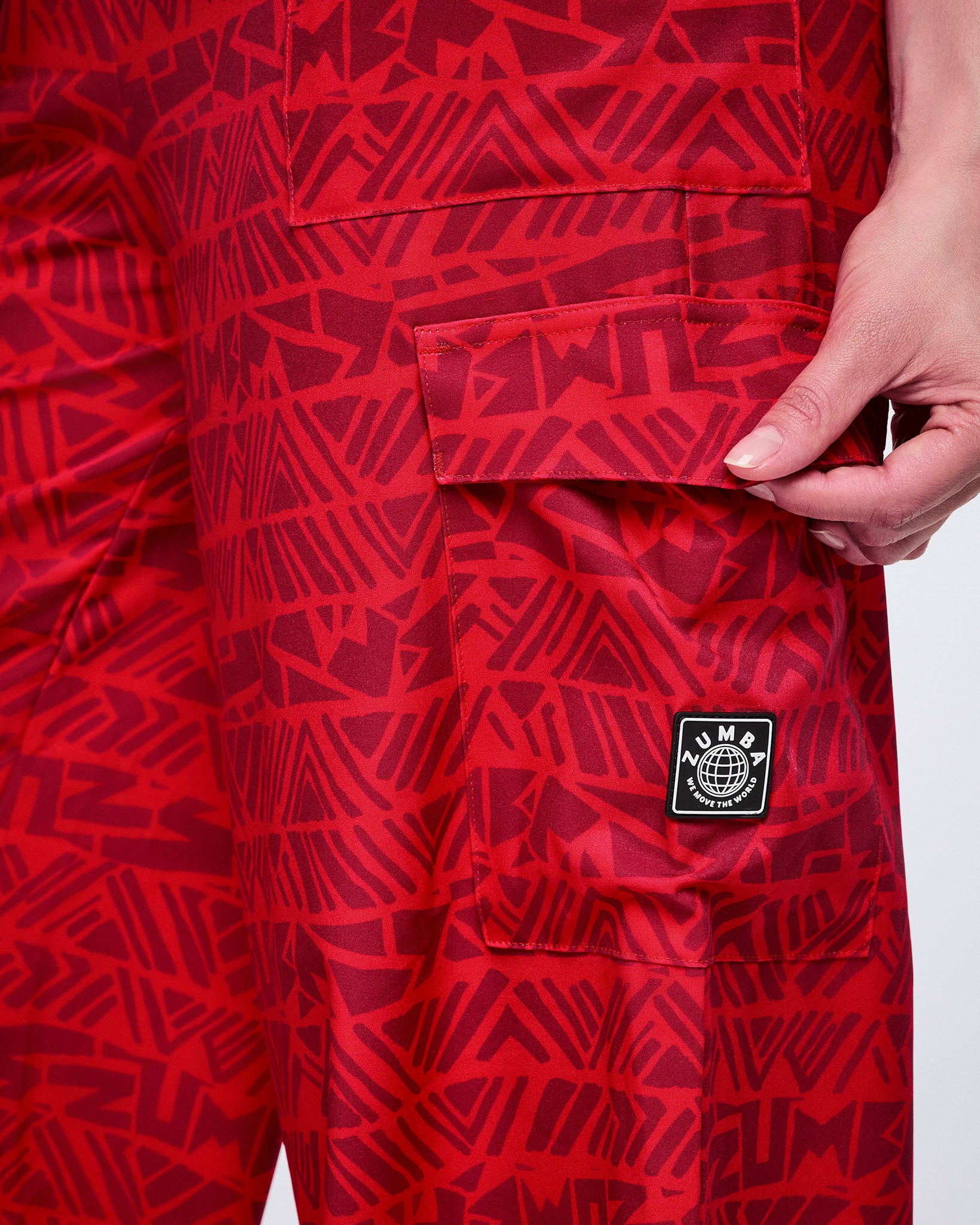 Close-up of wide-leg red cargo pants in a tonal geometric Zumba print, highlighting the flap cargo pocket and logo patch on the leg.