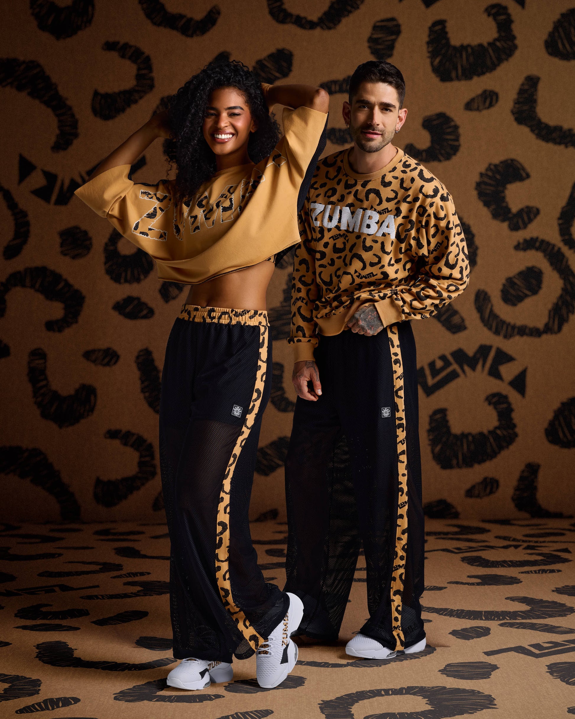 Female and male models wear mustard leopard-print Zumba tops, black mesh pants with side stripes, and white sneakers.